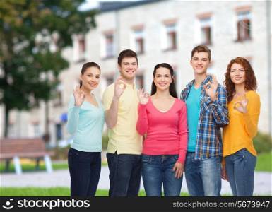 friendship, education, summer vacation and people concept - group of smiling teenagers showing ok sign over campus background