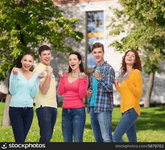 friendship, education, summer vacation, teamwork and people concept - group of smiling teenagers showing triumph gesture over campus background