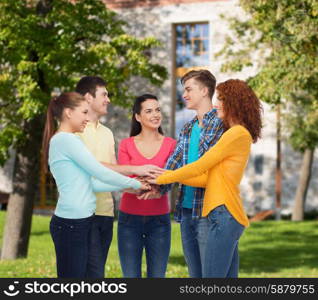 friendship, education, teamwork, gesture and people concept - group of smiling teenagers putting hand on top of each other over campus background