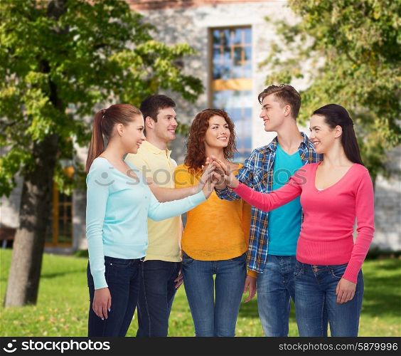 friendship, education, teamwork, gesture and people concept - group of smiling teenagers making high five over campus background
