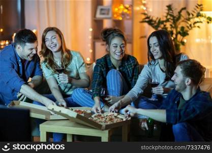 friendship, food and leisure concept - happy friends eating pizza and drinking non-alcoholic wine and watching tv at home in evening. friends eating pizza and drinking wine at home