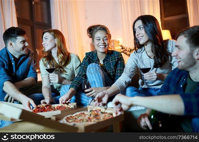 friendship, food and leisure concept - happy friends eating pizza and drinking non-alcoholic red wine at home in evening. friends eating pizza and drinking red wine at home