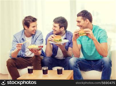 friendship, food and leisure concept - smiling friends with soda and hamburgers at home