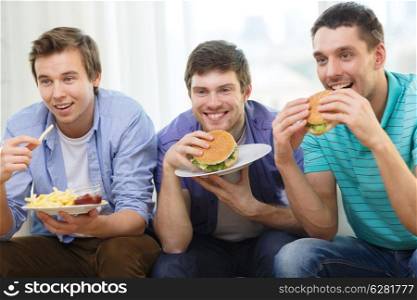 friendship, food and leisure concept - smiling friends with soda and hamburgers at home
