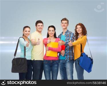 friendship, future, education and people concept - group of smiling teenagers with folders and school bags showing thumbs up over gray background with laser light
