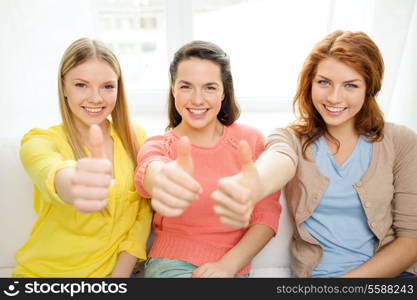 friendship, gesture and happiness concept - three girlfriends showing thumbs up at home