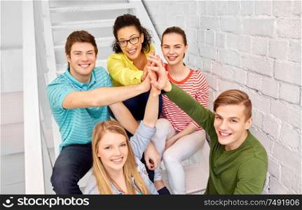 friendship, gesture and success concept - smiling teenage friends or students making high five on stairs. teenage friends or students making high five