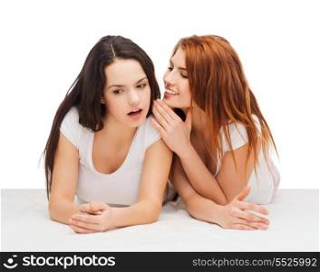 friendship, happiness and people concept - two smiling girls whispering gossip