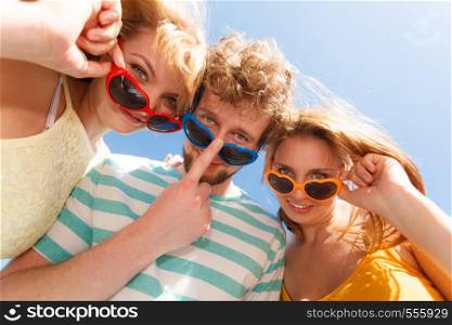 Friendship happiness summer freedom concept. Group of friends boy two girls in colorful sunglasses having fun outdoor, joy playful mood, wide angle view. Group friends boy two girls having fun outdoor