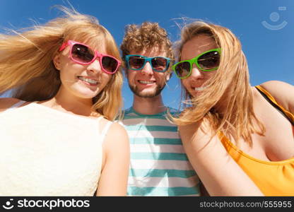 Friendship happiness summer holidays concept. Group of friends boy two girls in colorful sunglasses having fun outdoor against sky, joy playful mood.. Group friends boy two girls having fun outdoor