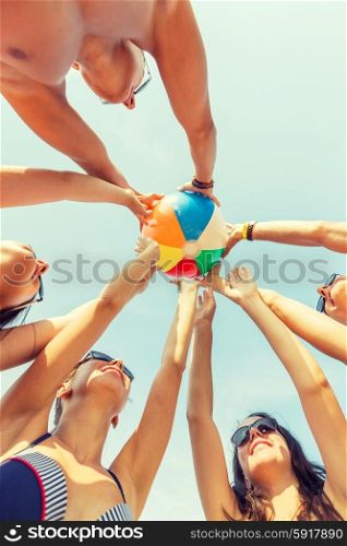 friendship, happiness, summer vacation, holidays and people concept - group of smiling friends wearing swimwear standing in circle with beach ball over blue sky