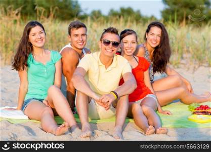 friendship, happiness, summer vacation, holidays and people concept - group of smiling friends sitting beach