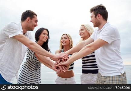 friendship, happiness, unity and people concept - smiling friends putting hands on top of each other