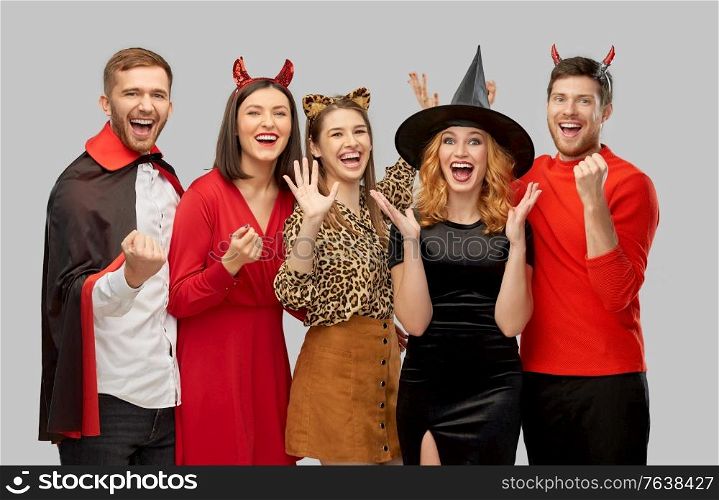 friendship, holiday and celebration concept - group of happy smiling friends in halloween costumes of vampire, devil, witch and leopard over grey background. happy friends in halloween costumes over grey