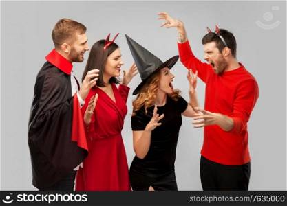 friendship, holiday and people concept - group of happy smiling friends in halloween costumes of vampire, devil, witch and cheetah scaring each other over grey background. friends in halloween costumes scaring each other
