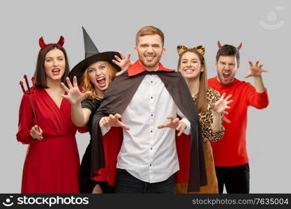 friendship, holiday and people concept - group of happy smiling friends in halloween costumes of vampire, devil, witch and leopard scaring over grey background. friends in halloween costumes scaring