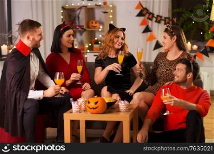 friendship, holiday and people concept - group of happy smiling friends in halloween costumes of vampire, devil, cat and cheetah with non-alcoholic drinks at home party at night. happy friends in halloween costumes at home party