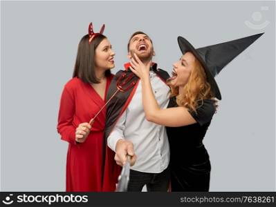 friendship, holiday and people concept - group of happy smiling friends in halloween costumes of witch, devil and vampire having fun taking picture by selfie stick over grey background. happy friends in halloween costumes taking selfie