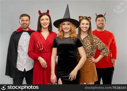 friendship, holiday and people concept - group of happy smiling friends in halloween costumes of vampire, devil, witch and leopard over grey background. happy friends in halloween costumes over grey