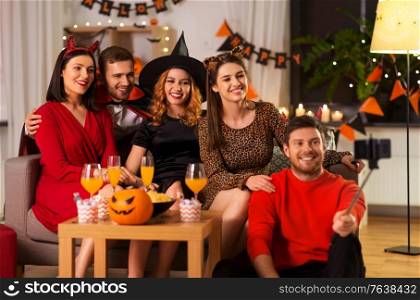 friendship, holiday and people concept - group of happy smiling friends in halloween costumes of vampire, devil, witch and cheetah taking picture by smartphone selfie stick at home party at night. happy friends in halloween costumes taking selfie