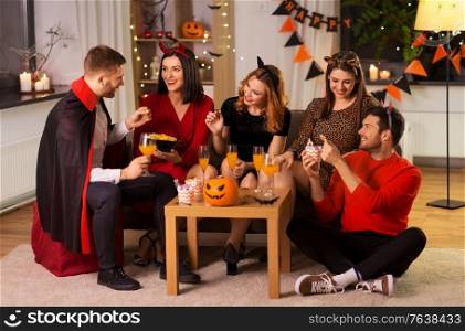 friendship, holiday and people concept - group of happy smiling friends in halloween costumes of vampire, devil, witch and cheetah at home party at night. happy friends in halloween costumes at home party