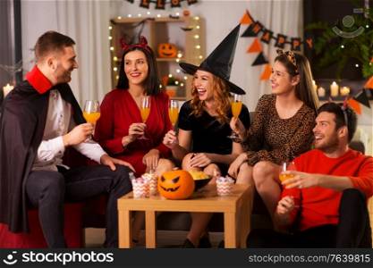 friendship, holiday and people concept - group of happy smiling friends in halloween costumes of vampire, devil, witch and cheetah with non-alcoholic drinks at home party at night. happy friends in halloween costumes at home party