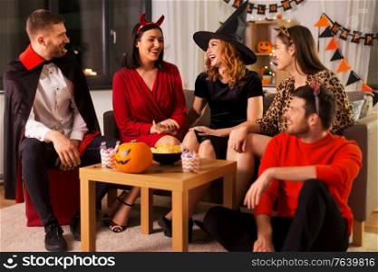 friendship, holiday and people concept - group of happy smiling friends in halloween costumes of vampire, devil, witch and cheetah at home party at night. happy friends in halloween costumes at home party