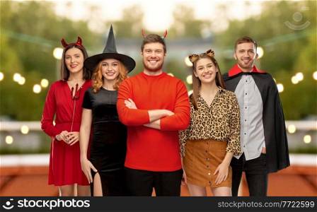 friendship, holiday and people concept - group of happy smiling friends in halloween costumes of v&ire, devil, witch and leopard over roof top party background. happy friends in halloween costumes at party