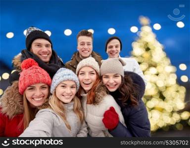 friendship, holidays and people concept - group of happy friends taking selfie outdoors over christmas lights background. happy friends taking selfie outdoors at christmas