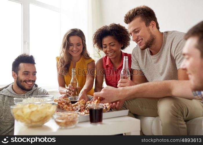 friendship, holidays, fast food and celebration concept - happy friends with drinks and snacks eating pizza at home