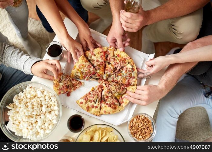 friendship, holidays, fast food and celebration concept - happy friends with drinks and snacks eating pizza at home. close up of people taking pizza slices at home
