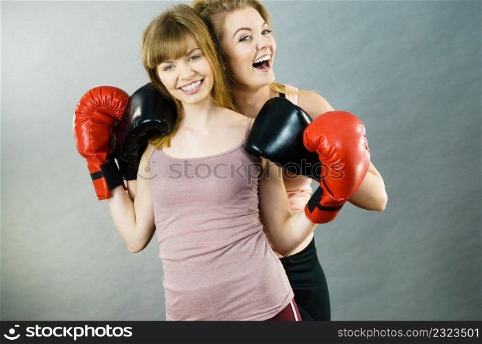 Friendship, human relations concept. Two happy women friends having fun smiling with joy wearing boxing gloves being fit and sporty.. Two women friends wearing boxing gloves