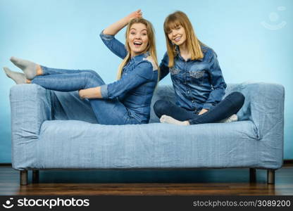 Friendship, human relations concept. Two happy women friends or sisters wearing jeans shirts sitting on sofa having fun.. Two happy women friends wearing jeans outfit