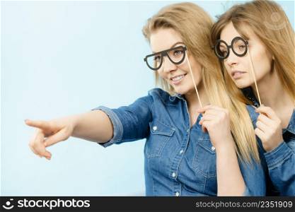 Friendship, human relations concept. Two happy women friends or sisters wearing jeans shirts pointing somewhere.. Two happy women friends wearing jeans outfit poitning