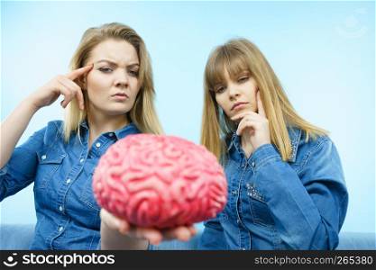 Friendship, human relations concept. Two women friends or sisters wearing jeans shirts, thinking about solving problem holding fake brain.. Two women friends thinking