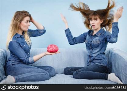 Friendship, human relations concept. Two women friends or sisters wearing jeans shirts, thinking about solving problem holding fake brain.. Two women friends thinking