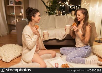 friendship, hygge and pajama party concept - happy female friends or teenage girls eating waffles and drinking cacao with marshmallow at home. happy female friends eating waffles at home