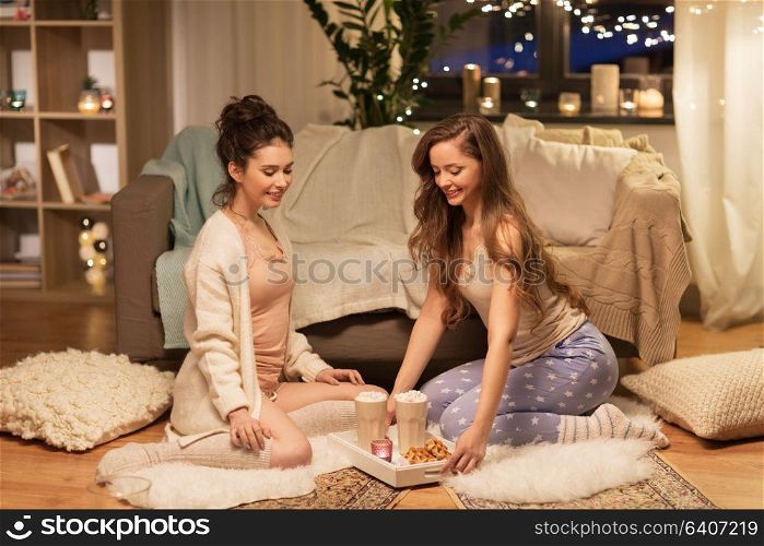 friendship, hygge and pajama party concept - happy female friends or teenage girls with cacao and waffles on tray at home. female friends with cacao and waffles at home