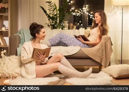 friendship, hygge and pajama party concept - happy female friends or teenage girls with book and sketchbook reading and drawing at home. female friends with book and sketchbook at home
