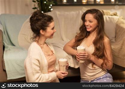 friendship, hygge and pajama party concept - happy female friends or teenage girls drinking cacao with marshmallow at home. happy female friends drinking cacao at home