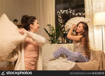 friendship, hygge and pajama party concept - happy female friends or teenage girls having pillow fight at home. happy female friends having pillow fight at home