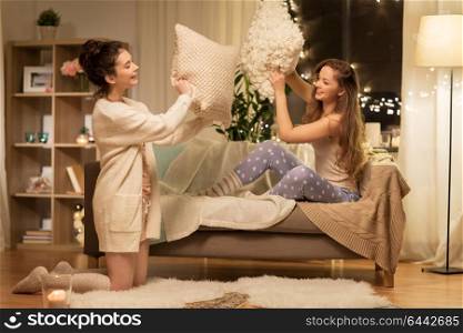 friendship, hygge and pajama party concept - happy female friends or teenage girls having pillow fight at home. happy female friends having pillow fight at home