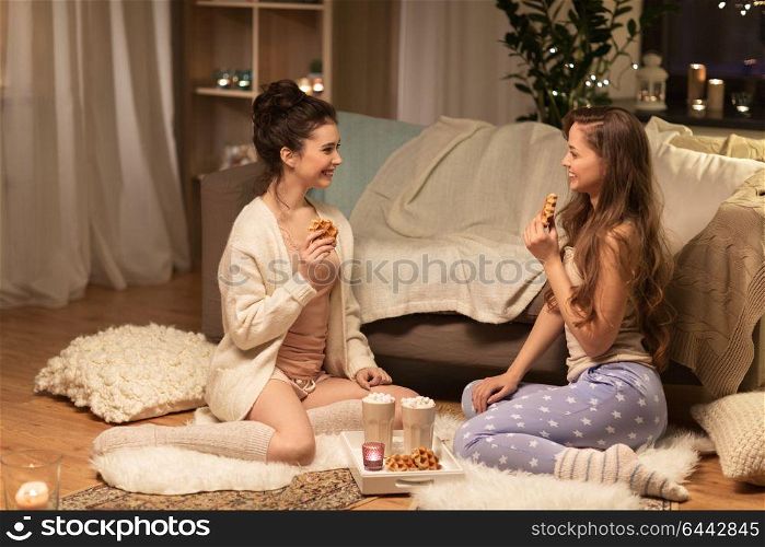 friendship, hygge and pajama party concept - happy female friends or teenage girls eating waffles with cacao at home. happy female friends eating waffles at home