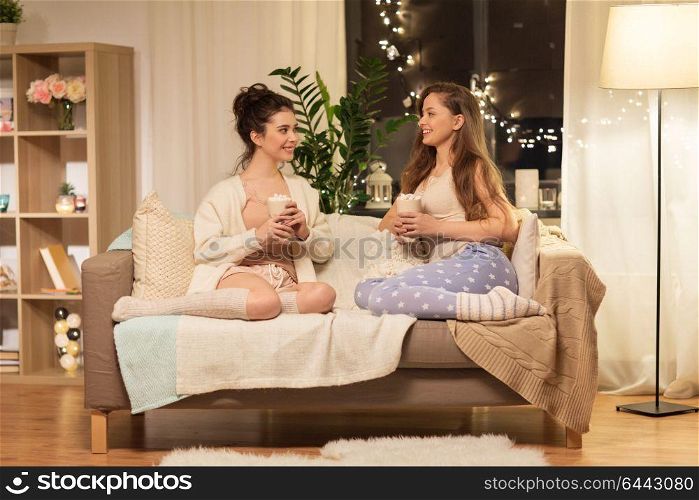 friendship, hygge and pajama party concept - happy female friends or teenage girls drinking cacao with marshmallow at home. happy female friends drinking cacao at home