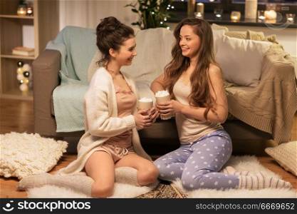 friendship, hygge and pajama party concept - happy female friends or teenage girls drinking cacao with marshmallow at home. happy female friends drinking cacao at home. happy female friends drinking cacao at home