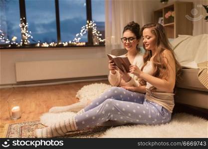 friendship, hygge and pajama party concept - happy female friends or teenage girls reading book at home. happy female friends reading book at home. happy female friends reading book at home