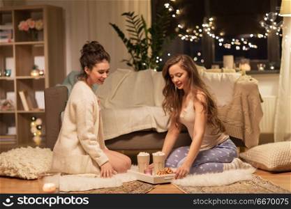 friendship, hygge and pajama party concept - happy female friends or teenage girls with cacao and waffles on tray at home. female friends with cacao and waffles at home. female friends with cacao and waffles at home