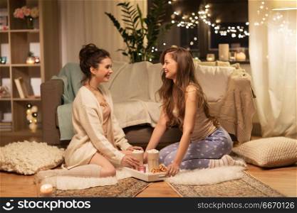 friendship, hygge and pajama party concept - happy female friends or teenage girls with cacao and waffles on tray at home. female friends with cacao and waffles at home. female friends with cacao and waffles at home