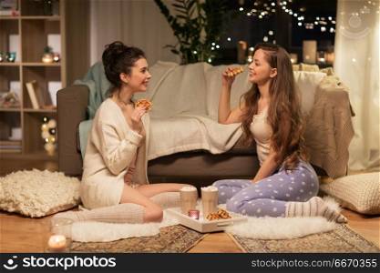friendship, hygge and pajama party concept - happy female friends or teenage girls eating waffles with cacao at home. happy female friends eating waffles at home. happy female friends eating waffles at home