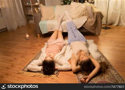 friendship, hygge and pajama party concept - happy female friends or teenage girls lying on floor at home. happy female friends at home pajama party